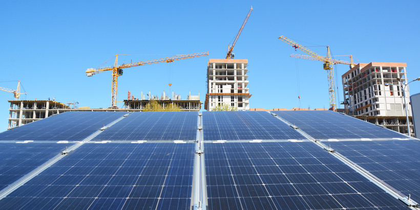 Green energy from solar cell harvesting sun light with cranes on the construction site background as modern global construction industry concept