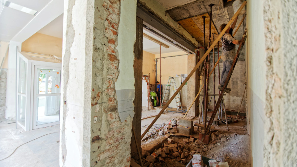 Renovation work inside a building. To the left you see the finished parts, to the right you see a man on a ladder, working with the wall.