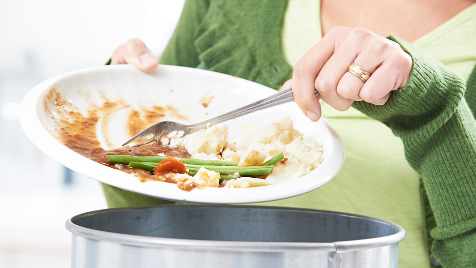 Woman scraping food leftovers into garbage bin